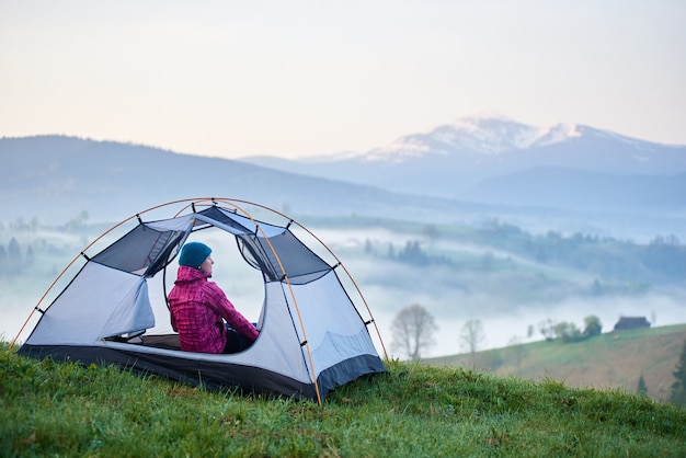 Rückansicht des weiblichen Wanderers, der im offenen Touristenzelt sitzt