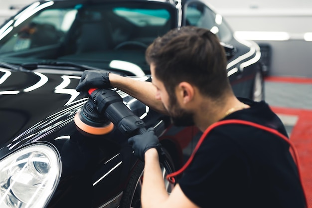 Rückansicht des weißen Mannes, der kauert und die Vorderseite des schwarzen Autos mit einem professionellen Pufferwerkzeugauto poliert