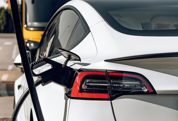 Rückansicht des weißen Tesla-Autos, das an der Ladestation für Elektrofahrzeuge aufgeladen wird