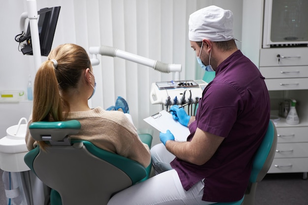 Rückansicht des Zahnarztes, der eine schwangere Frau berät, die im Zahnarztstuhl in der Zahnarztpraxis sitzt