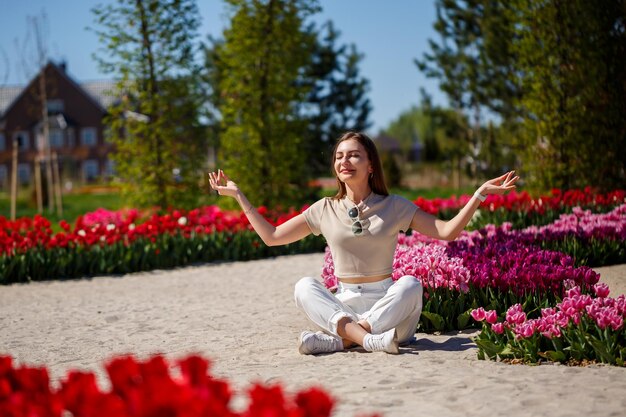 Rückansicht einer anonymen Frau in Sommerkleid und Hut, die an einem sonnigen Tag in der Natur in der Nähe blühender Tulpen auf einer Wiese spaziert