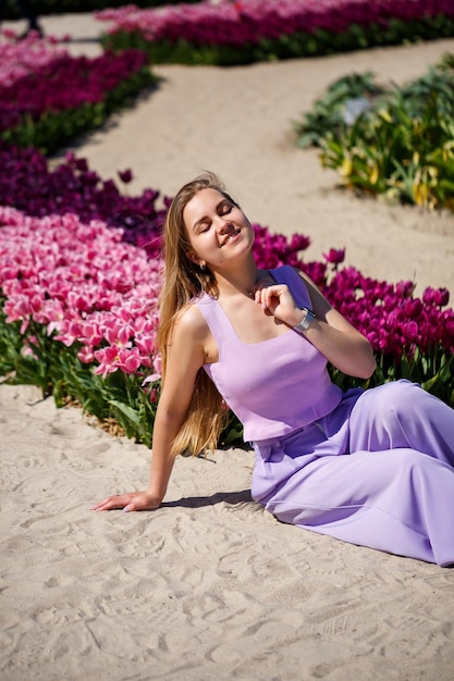 Rückansicht einer anonymen Frau in Sommerkleid und Hut, die an einem sonnigen Tag in der Natur in der Nähe blühender Tulpen auf einer Wiese spaziert