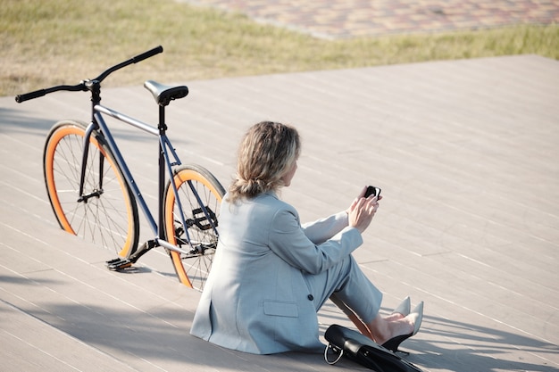 Rückansicht einer eleganten Geschäftsfrau, die im Smartphone scrollt