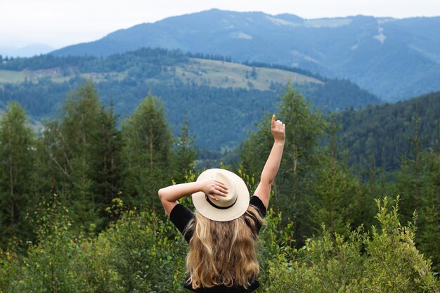 Rückansicht einer Frau, die ihre Hände vor dem Hintergrund der Berglandschaft hochhält. Freiheitskonzept