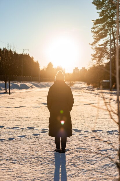 Rückansicht einer Frau, die im Schnee steht und Sonnenlicht betrachtet Ruhige Winteratmosphäre Zeit allein verbringen