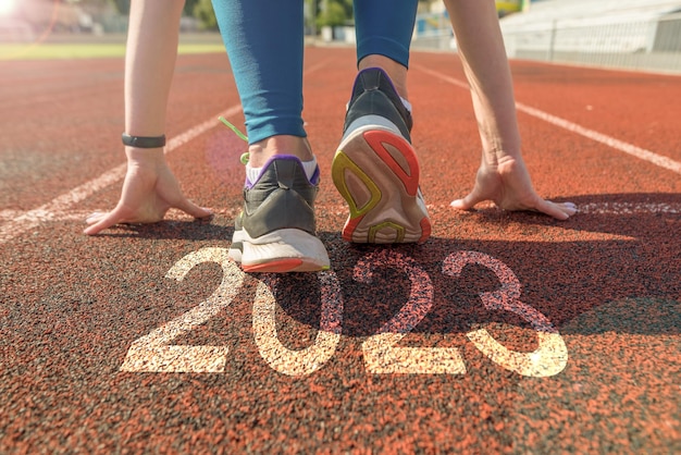 Rückansicht einer Frau, die sich auf den Start auf einer Leichtathletikbahn vorbereitet, auf der das Jahr 2023 eingraviert ist