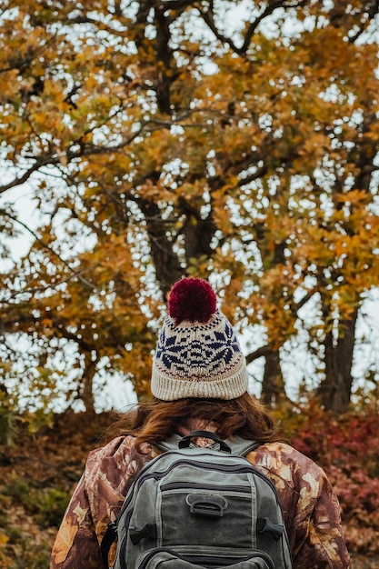 Rückansicht einer Frau mit Hut und Jacke mit Rucksack vor dem Hintergrund einer Herbstlandschaft