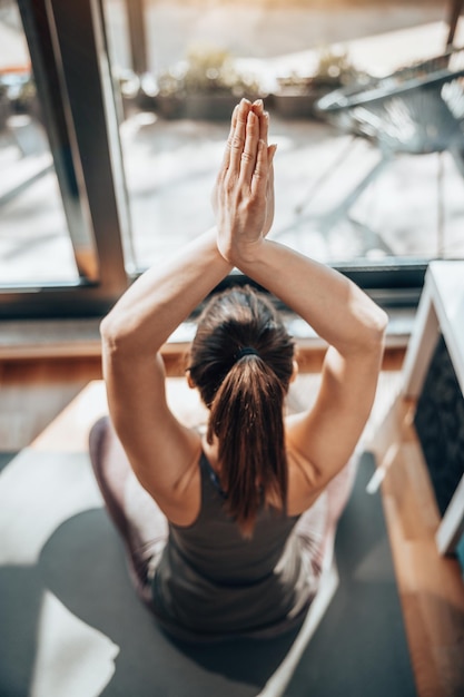 Rückansicht einer jungen süßen Frau, die morgens zu Hause in der Yoga-Position meditiert.