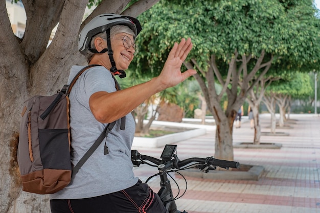 Rückansicht einer lächelnden Radfahrerin im Stadtpark mit Helm und Rucksack, die mit einem Elektrofahrrad läuft Konzept eines gesunden Lebensstils und nachhaltiger Mobilität