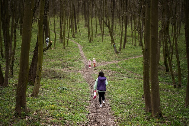 Rückansicht einer Mutter mit drei Kindern, die auf einem Waldweg spaziert. Frühlingsfreizeitkonzept im Freien