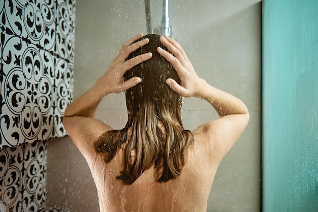 Rückansicht einer nackten Frau, die in einer Duschkabine duscht Frau, die morgens ihre Haare im Badezimmer wäscht h