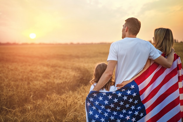 Rückansicht einer nicht erkennbaren glücklichen Familie im Weizenfeld mit amerikanischer Flagge