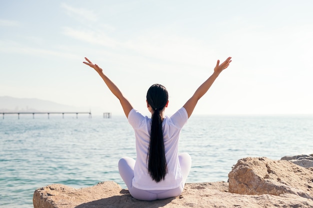 Rückansicht einer nicht erkennbaren jungen Frau, die Yoga am Meer macht, Konzept der Spiritualität und Entspannung