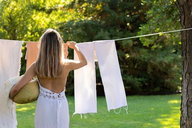 Foto rückansicht einer nicht erkennbaren jungen frau im boho-outfit, die die wäsche im sommergarten aufhängt