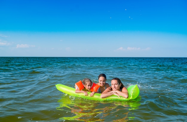 Rückansicht einer positiven jungen Familienmutter und zweier kleiner Töchter schwimmen an einem sonnigen Sommertag im Urlaub auf einer gelben Luftmatratze im Meer. Entspannungskonzept. Exemplar