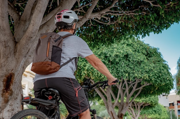Rückansicht einer Radfahrerin im Stadtpark mit Helm und Rucksack, die mit einem Elektrofahrrad läuft Konzept eines gesunden Lebensstils und nachhaltiger Mobilität