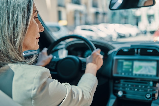 Rückansicht einer reifen schönen Frau in intelligenter Freizeitkleidung, die beim Autofahren lächelt