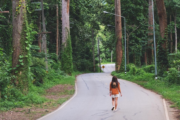 Rückansicht einer Reisenden, die die Straße entlang in den Wald geht