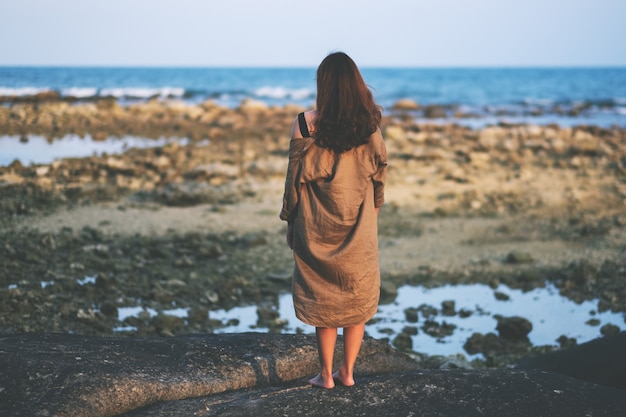 Rückansicht einer schönen asiatischen Frau, die allein am Strand an der Küste steht