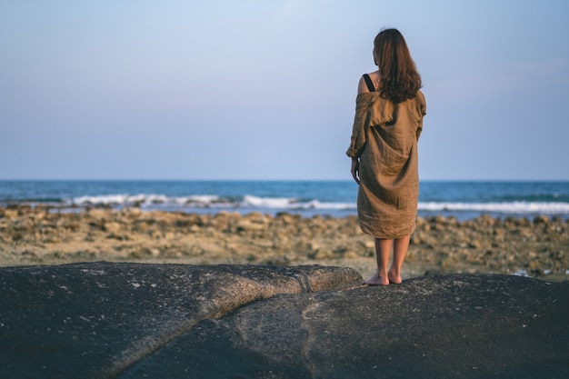 Rückansicht einer schönen asiatischen Frau, die allein am Strand an der Küste steht