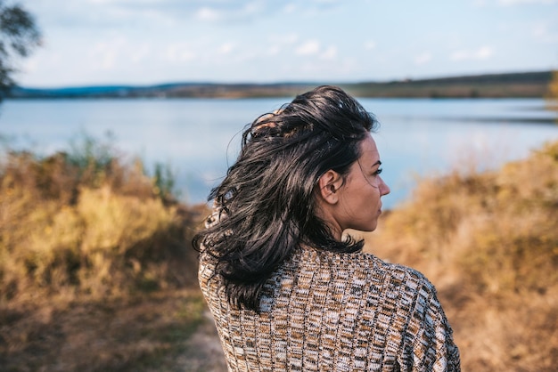 Rückansicht einer schönen Frau mit wehenden Haaren, die sich entspannt und die Natur neben dem See im Freien genießt Kaukasische verträumte Frau, die im Park mit Kopierraum und für das Hintergrundkonzept posiert