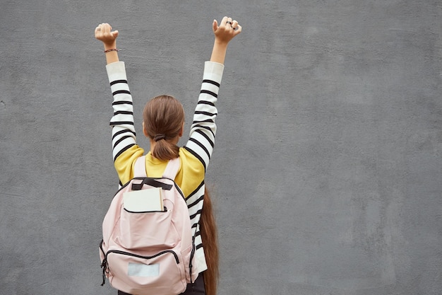 Foto rückansicht einer studentin mit rosafarbenem rucksack, der die hände isoliert auf grauem hintergrund hält