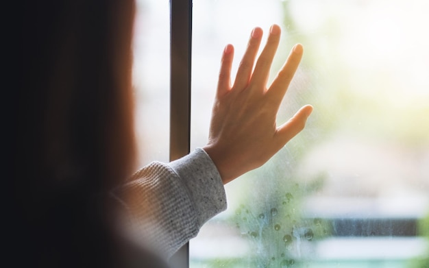 Rückansicht einer traurigen Frau, die ein Fenster berührt, während sie nach draußen schaut