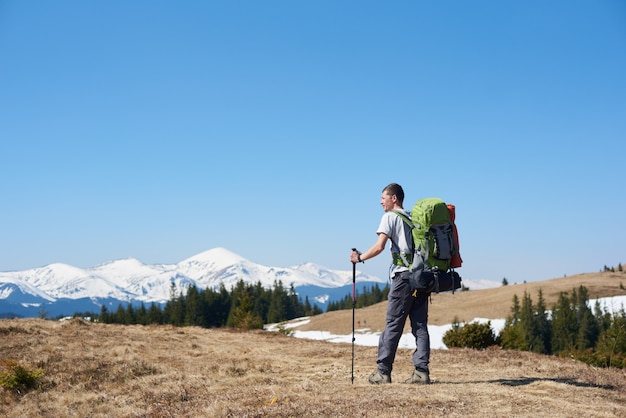 Rückansicht eines abenteuerlustigen Mannes mit Wanderausrüstung unter Verwendung von Trekkingstöcken beim Gehen auf dem Berg