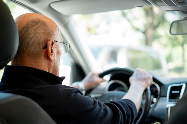 Rückansicht eines älteren kaukasischen Mannes mit den Händen über dem Lenkrad, der sein Auto fährt