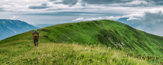 Rückansicht eines aktiven Mannes, der mit Campingausrüstung auf einer Bergkette spaziert