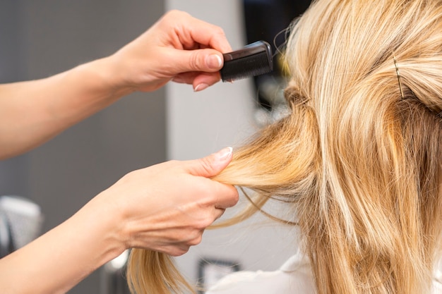 Rückansicht eines Friseurs kämmt blondes Haar der jungen Frau in einem Schönheitssalon