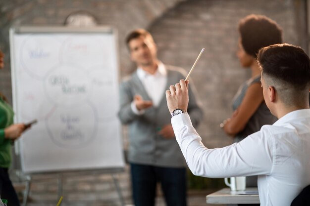 Foto rückansicht eines geschäftsmannes, der an einem seminar teilnimmt und den arm hebt, um die frage im büro zu beantworten