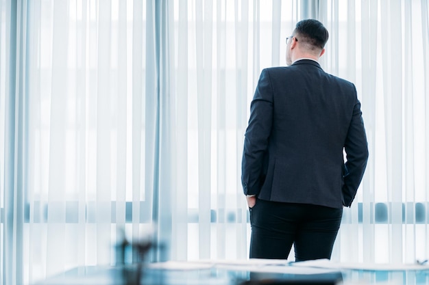 Rückansicht eines Geschäftsmannes, der im Büro steht und aus dem Fenster schaut. kurze Arbeitspause, um Gedanken zu sammeln