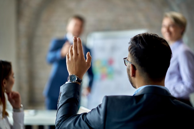 Rückansicht eines Geschäftsmannes, der seine Hand hebt, um die Frage während einer Geschäftspräsentation im Büro zu stellen