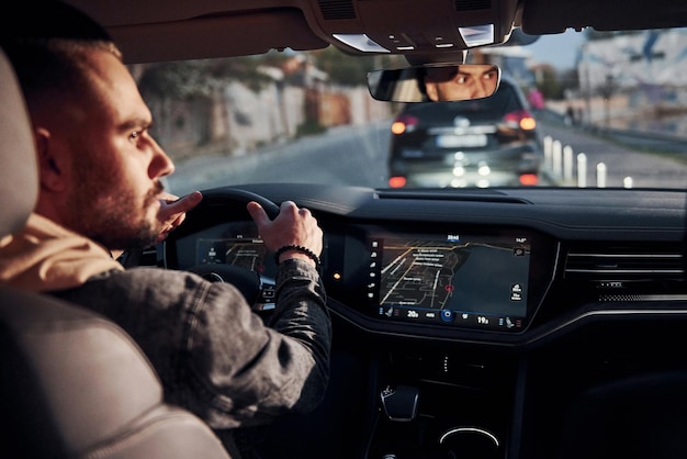 Rückansicht eines gutaussehenden unrasierten Mannes in modischer Kleidung, der mit seinem Auto fährt