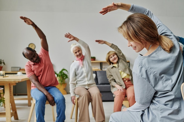 Rückansicht eines jungen Ausbilders, der beim morgendlichen Training zusammen mit älteren Menschen Übungen macht