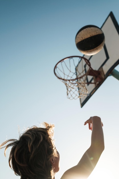 Rückansicht eines Jungen, der an einem sonnigen Tag auf dem Sportplatz einen Ball in den Korb wirft, während er Basketball spielt