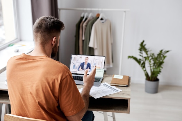 Rückansicht eines jungen Mannes, der vor einem Laptop mit Tutor auf dem Bildschirm sitzt