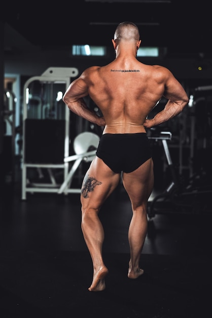 Rückansicht eines jungen muskulösen Bodybuilders, der seine perfekten Rückenmuskeln zeigt, während er nach dem Training im Fitnessstudio posiert.