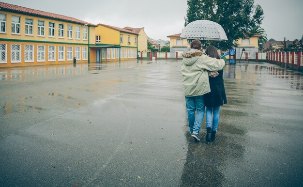 Rückansicht eines jungen Paares, das sich unter dem Regenschirm an einem regnerischen Herbsttag umarmt. Liebes- und Paarbeziehungskonzept.