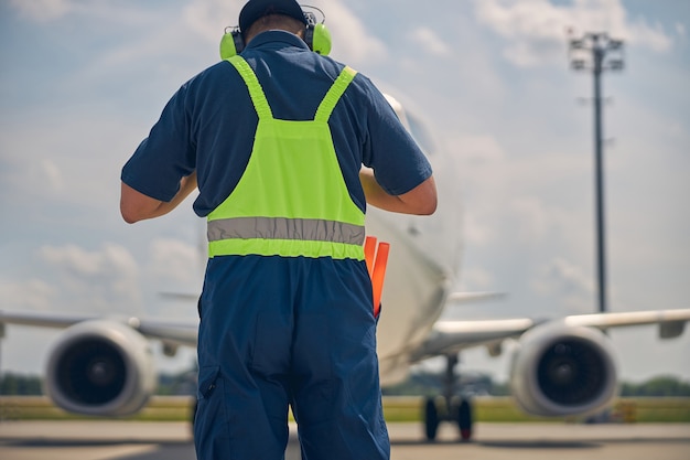 Rückansicht eines kaukasischen Flugzeugmarschallers, der vor dem gelandeten Zivilflugzeug steht