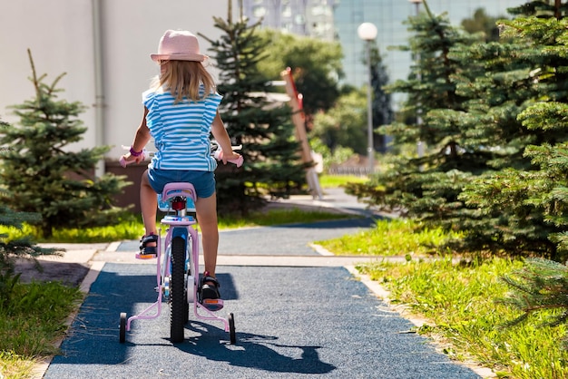 Rückansicht eines kleinen kindes mit sommerhut, das draußen im stadtpark fahrrad fährt