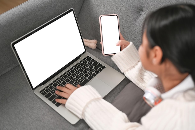 Rückansicht eines Mädchens mit Laptop und Smartphone, während es auf dem Sofa liegt