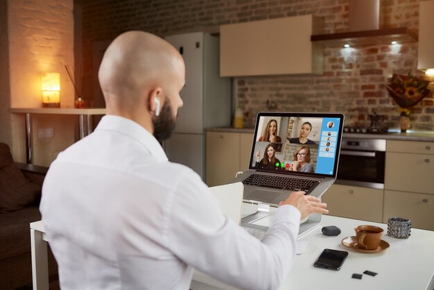 Rückansicht eines männlichen Angestellten in Kopfhörern, der auf einer Geschäftsvideokonferenz auf einem Laptop erklärt und gestikuliert.