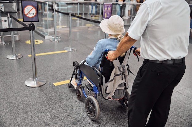 Rückansicht eines männlichen Flughafenangestellten, der eine behinderte Reisende zu einem Flugzeug transportiert