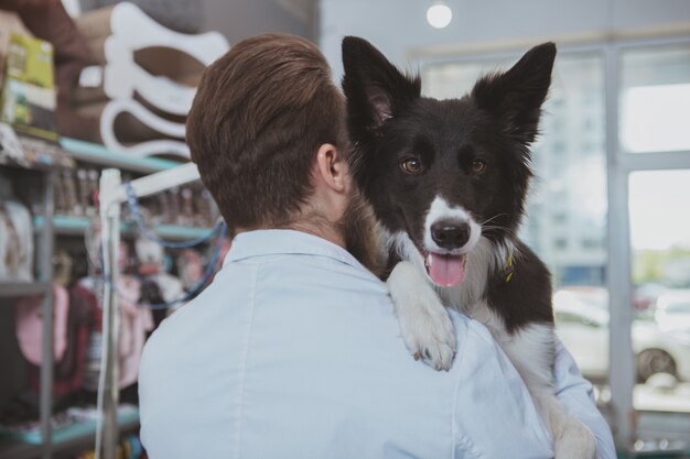 Rückansicht eines männlichen Tierarztes, der entzückenden glücklichen Hund trägt