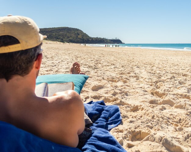 Foto rückansicht eines mannes, der an einem strand sitzt und ein buch in einem sonnigen tag liestcopy spacelifestyle-konzept