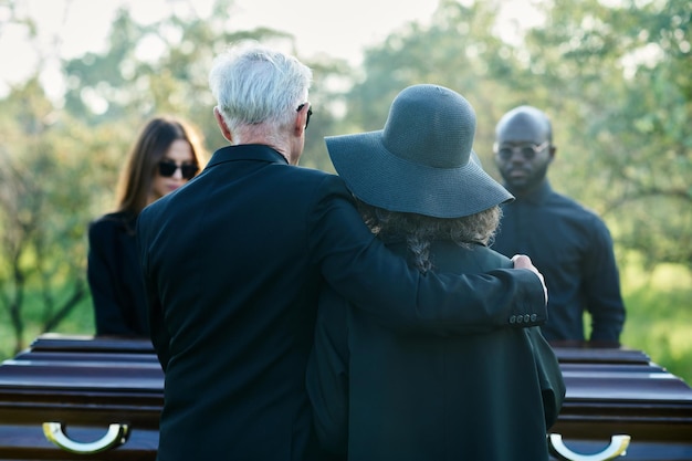 Rückansicht eines reifen grauhaarigen Mannes, der seine Frau mit schwarzem Hut umarmt