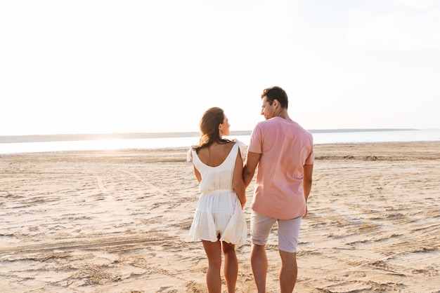 Rückansicht eines schönen jungen Paares, das Sommerkleidung trägt, die am Strand steht