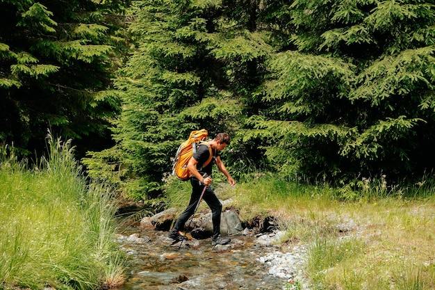 Rückansicht eines touristischen jungen Mannes mit Rucksack reist durch den Wald in der Nähe des Flusses